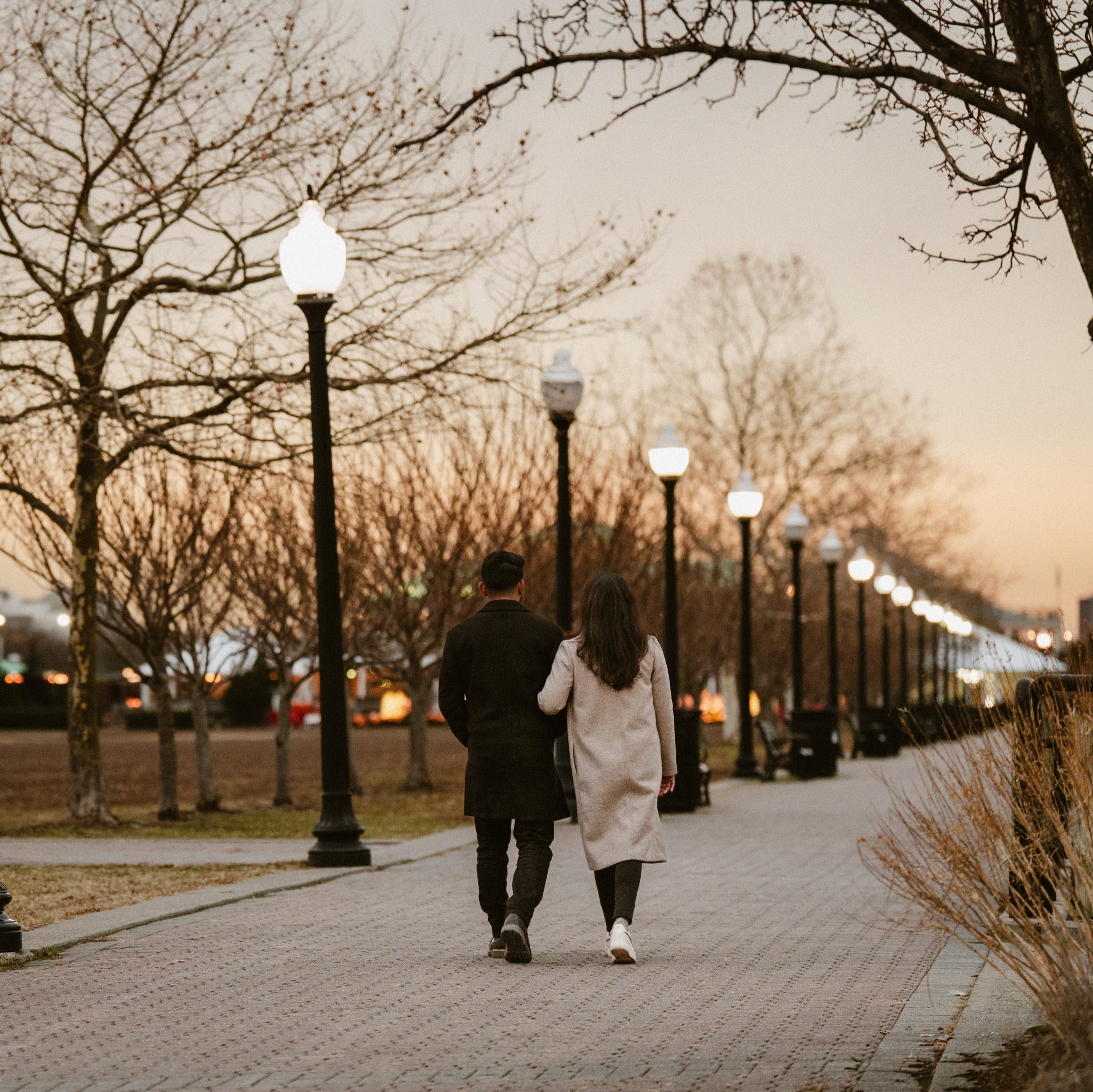 Walking together down a lamplit riverside path at dusk